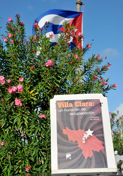 Libro Villa Clara: un huracán de recuperación, y bandera cubana al fondo.