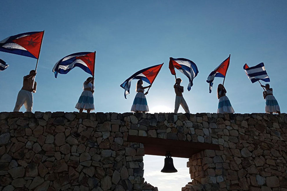 Jóvenes con banderas cubans en el muro de La Demajagua.