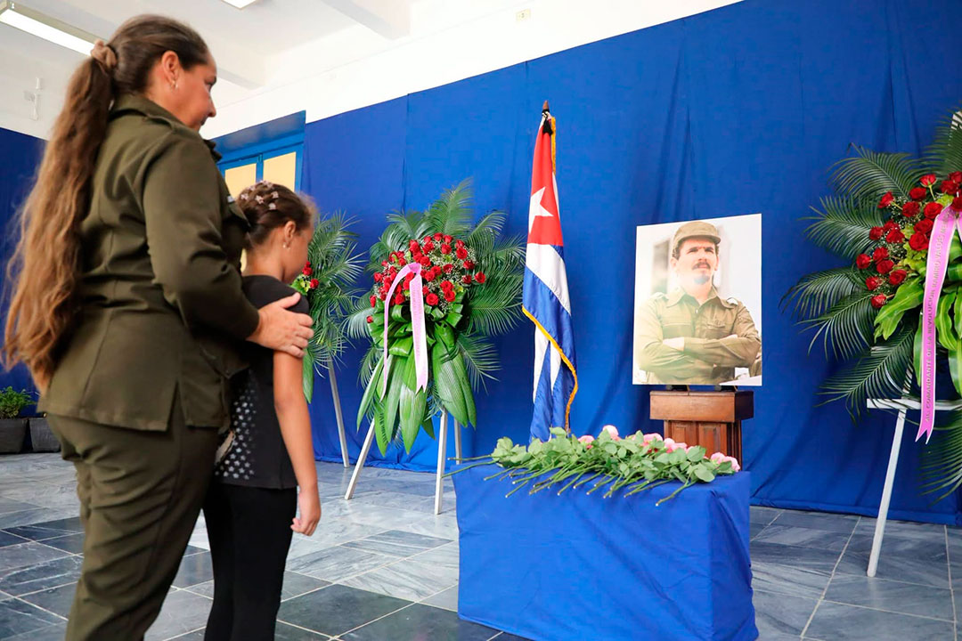 Mujer militar con su hija rinden homenaje a Ramiro Valdés.