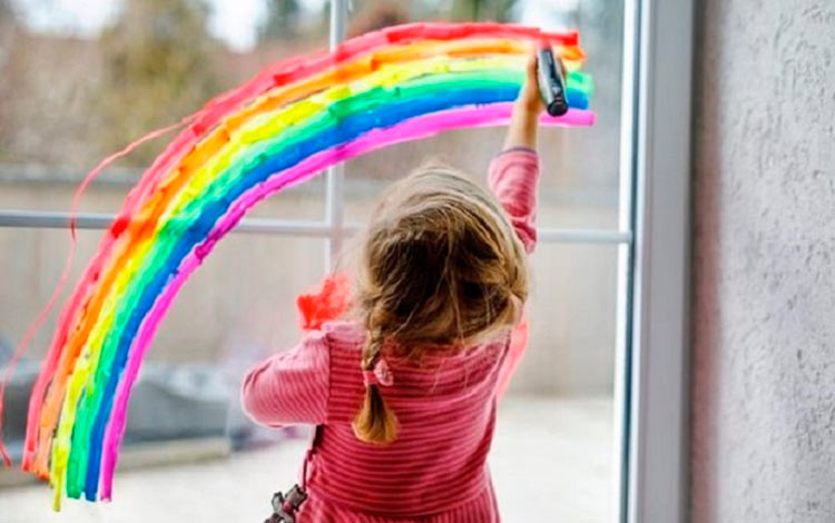 Niña pinta un arcoíris en la ventana.